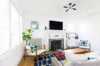 Madison Valley Design: A bright living room features a white tiled fireplace with a television mounted above, mid-century modern armchairs, and a bold blue patterned rug