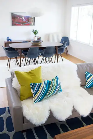 Madison Valley Design: A mid-century modern living room features a gray sofa topped with a plush white sheepskin rug and colorful pillows