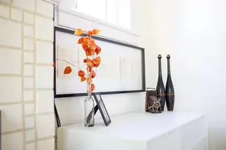 Madison Valley Design: A white sideboard styled with vintage decor, featuring framed line-art prints, dried orange physalis in a glass bottle, an antique folding camera