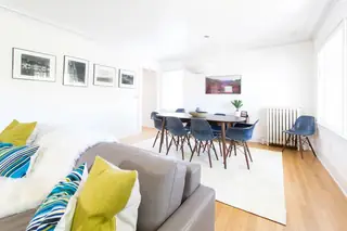 Madison Valley Design: A bright, open-plan space featuring a grey leather sofa in the foreground and a dining table surrounded by blue shell chairs under a pendant light