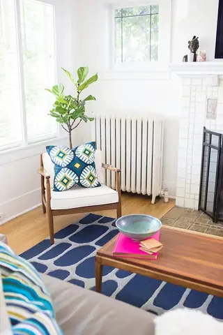 Madison Valley Design: A bright mid-century modern living room features a wooden armchair with a geometric cushion, a blue patterned rug, and a wooden coffee table