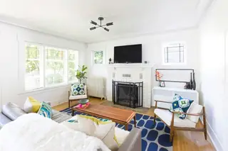 Madison Valley Design: A bright mid-century modern living room featuring a tiled fireplace, blue patterned rug, and stylish wooden accent chairs
