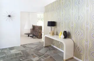 Pebble Beach Drive, Palm Springs: A mid-century modern entryway features flagstone flooring, retro wavy wallpaper, and a curved cream console table positioned under a dark lamp