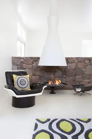 Pebble Beach Drive, Palm Springs: A modern living space features a striking white conical hanging fireplace set against a rustic stone wall