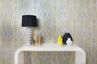 Pebble Beach Drive, Palm Springs: A retro white console table is styled with a black table lamp, decorative ceramics, and bookends against a bold wavy yellow and gray wallpaper