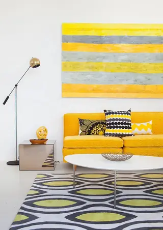 Pebble Beach Drive, Palm Springs: A bright mid-century modern living room features a yellow sofa with decorative pillows underneath a large yellow and gray striped painting