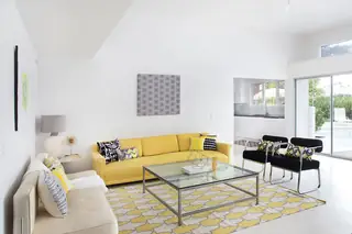 Pebble Beach Drive, Palm Springs: A bright, modern living room features a vibrant yellow sofa, glass coffee table, geometric patterned rug, and black accent chairs set