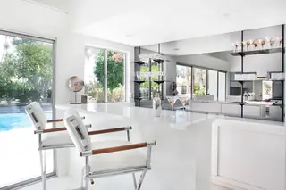 Pebble Beach Drive, Palm Springs: A sleek white modern home bar features chrome-framed bar stools with wooden armrests, set against a mirrored wall