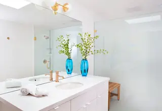 Pebble Beach Drive, Palm Springs: A bright modern bathroom vanity features gold hardware, a large mirror, and a vibrant blue vase filled with green branches