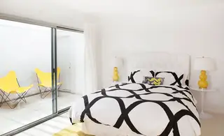 Pebble Beach Drive, Palm Springs: A bright modern bedroom features a black-and-white geometric duvet, yellow gourd table lamps, and a sliding glass door leading to a patio