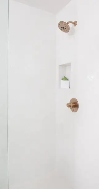Pebble Beach Drive, Palm Springs: A minimalist modern shower with white arabesque tiled walls features warm brushed-brass fixtures and a small built-in wall niche