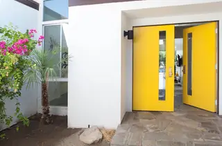 Pebble Beach Drive, Palm Springs: A pair of vibrant yellow double front doors with slender glass windows open into a modern home's entryway featuring stone tile flooring