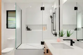 A modern white bathroom features a glass-enclosed tub shower combination with matte black fixtures and a sleek vanity.
