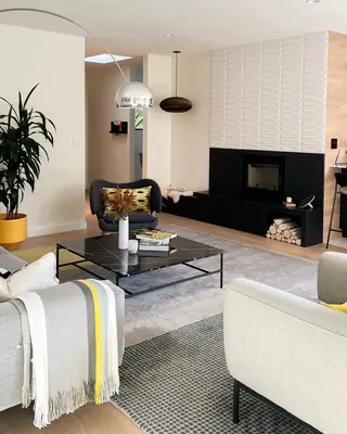 A modern living room featuring a black marble coffee table, a sleek fireplace with textured white wall panels, and yellow accent decor.