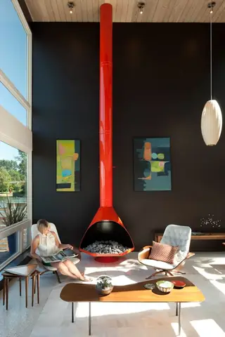 The Aqua Lair, Lake Sammamish: A mid-century modern living room featuring a striking bright red freestanding cone fireplace against a dark accent wall with retro lounge chairs