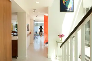 The Aqua Lair, Lake Sammamish: A bright mid-century modern hallway features an open vibrant orange front door framing a scenic lake view, adjacent to a white staircase