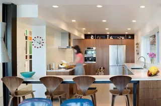The Aqua Lair, Lake Sammamish: A mid-century modern open-plan kitchen features warm walnut cabinetry, a white counter breakfast bar with curved wooden barstools