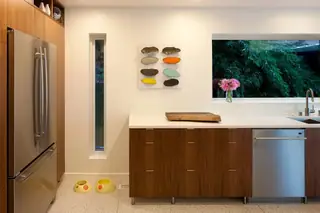 The Aqua Lair, Lake Sammamish: A mid-century modern kitchen features warm walnut cabinetry, stainless steel appliances, terrazzo flooring
