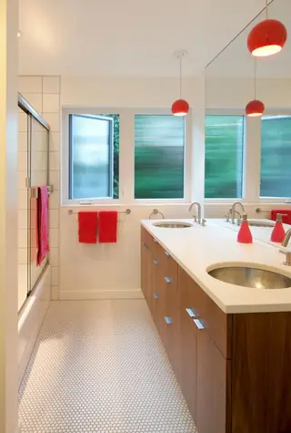 The Aqua Lair, Lake Sammamish: A modern bathroom features a long wooden double vanity with a white countertop, mosaic penny tile flooring, and vibrant red pendant lights