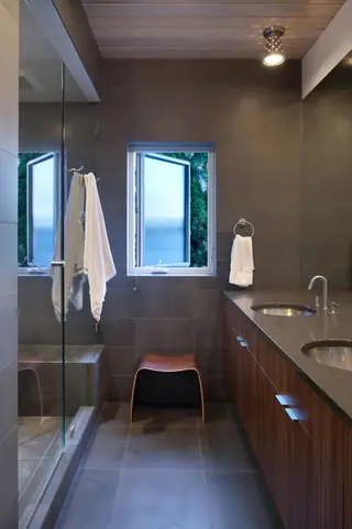 The Aqua Lair, Lake Sammamish: A sleek modern bathroom featuring dark gray tiled walls, a warm wood double vanity, a glass shower enclosure