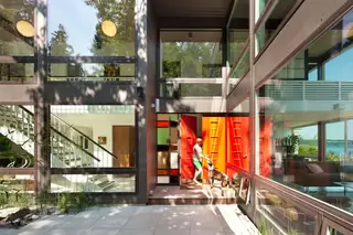 The Aqua Lair, Lake Sammamish: A woman and her dog stand at the open bright orange front door of a mid-century modern house featuring expansive glass windows
