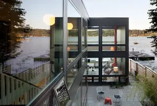 The Aqua Lair, Lake Sammamish: A high-angle exterior view of a modern lake house featuring expansive floor-to-ceiling glass windows and a paved outdoor patio