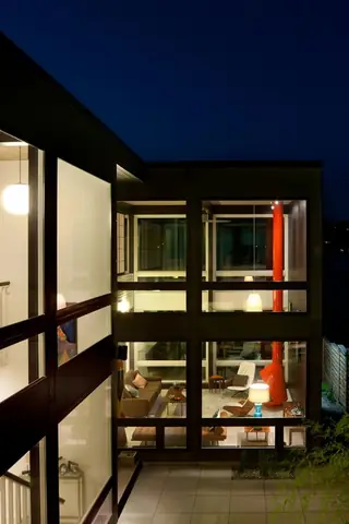 The Aqua Lair, Lake Sammamish: An exterior night view of a mid-century modern home with large glass windows revealing warmly lit multi-level living spaces