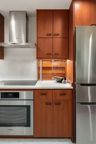 A mid-century modern kitchen featuring rich warm wood cabinetry, white countertops, and sleek stainless steel appliances.