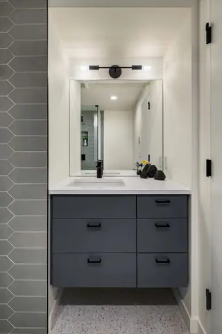 A modern bathroom niche features a dark gray floating vanity with a white countertop, black fixtures, and an adjacent gray chevron tile wall.