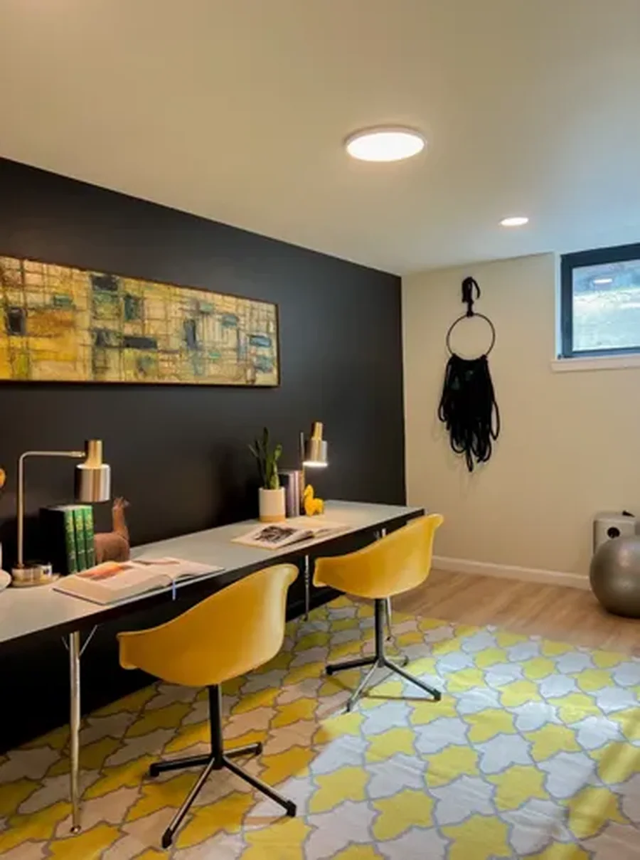 Home office with white desk and yellow swivel chairs against dark accent wall